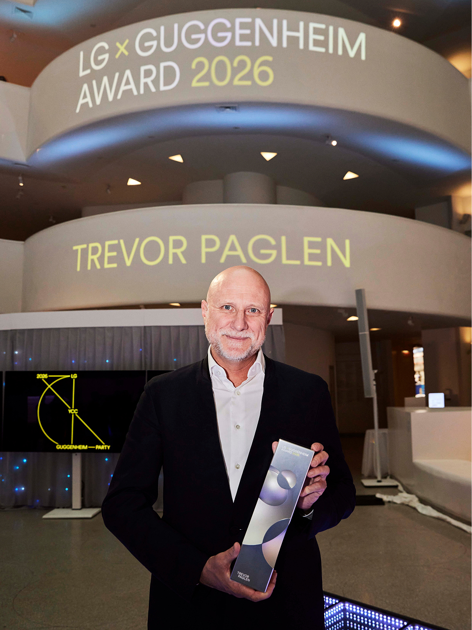 Trevor Paglen posing for a commemorative photo with his name projected on the Guggenheim Museum rotunda wall